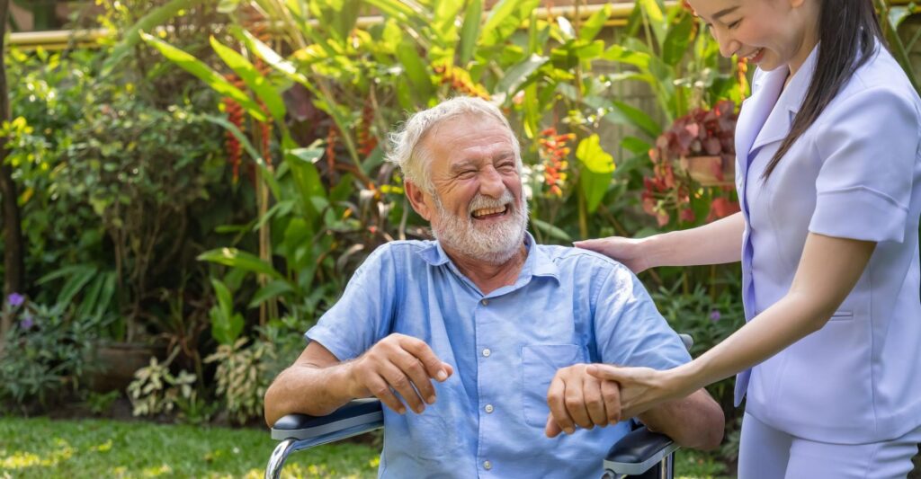Man in a wheelchair laughing with a support worker in a garden