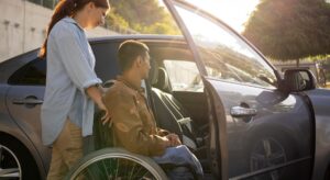 Support worker assisting a man in a wheelchair to enter a car
