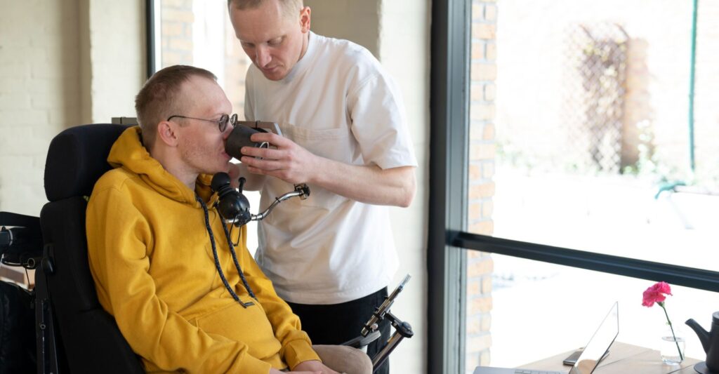 Support worker assisting a man in a wheelchair with a drink