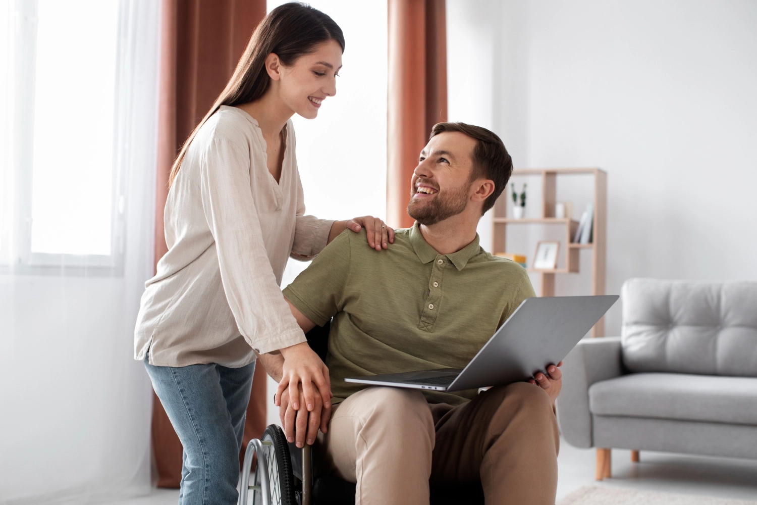 Smiling man in wheelchair using laptop at home.