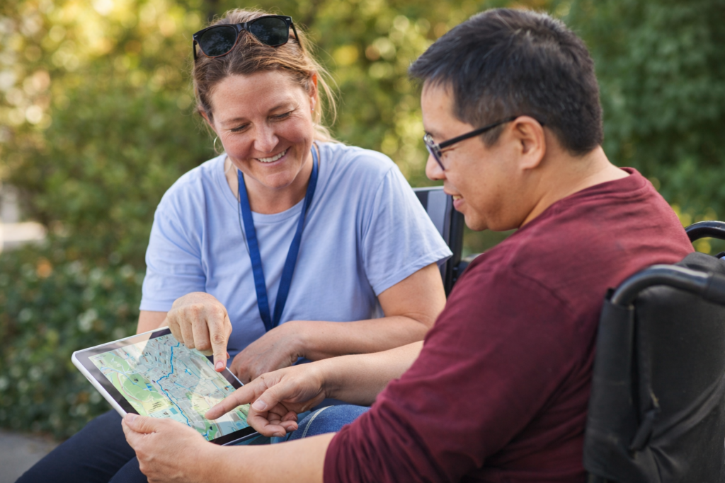A support worker and a participant looking at a map or a tablet together, planning a trip.
