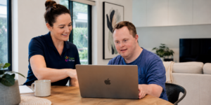 A friendly professional ndis support worker helping an Australian participant review their plan options on a laptop.